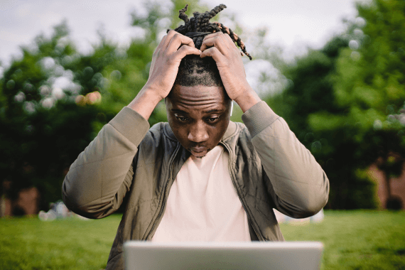 Frustrated man with hands on head looks at computer in shock